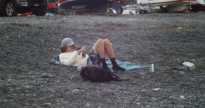 Young Male Relaxing And Using Smartphone Outdoor Near Porthallow Fishing Village In Cornwall, England, United Kingdom - wide shot