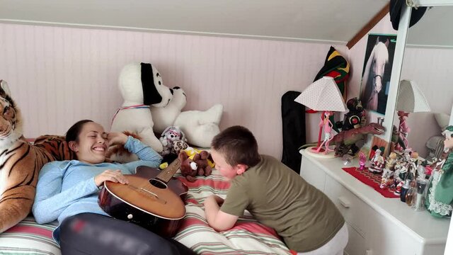 Mother playing guitar together with autistic son - Mother laying on bed interacting with happy boy - Tiptoeing and hand flapping stereotypic movements