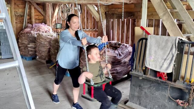 Mom pushing autistic son in swing inside barn - Having a good time together - Boy flapping doing stereoptypic movements like hand flapping when laughing