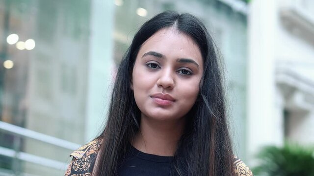 Close up shot of beautiful young woman smiling while looking at camera near a shopping mall. Smiling Indian girl UHD video