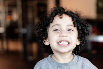 close-up portrait of a smiling white latin minor boy with black curls, inside a fast food establishment.