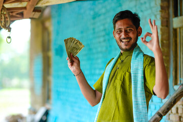 Happy Indian farmer showing money at home.