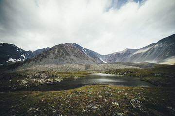 Scenic mountain landscape with glacial lake among mountains under gray cloudy sky. Atmospheric alpine scenery with transparent mountain lake in rainy weather. Beautiful clear alpine lake among rocks.