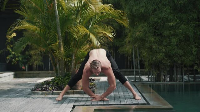 Fitness caucasian sporty man doing yoga and stretching muscles. Strong guy does exercises and asana outdoor at the poolside in nature. Healthy lifestyle concept. High quality 4k footage video.