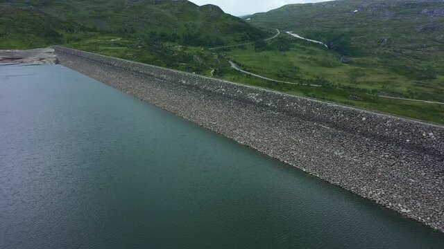 Top view inside water reservoir Sysendammen in Hardangervidda National Park Norway - Aerial showing stored water and top of massive dam with road rv7 in background