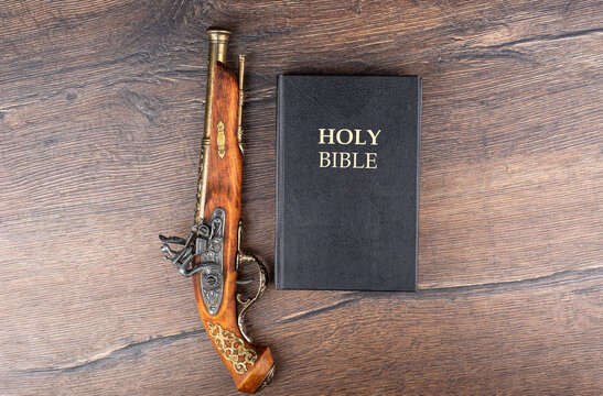 Holy Bible and old powder pistol on wooden background.