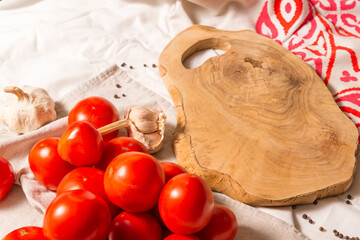Cutting board made of olive tree, next to a bunch of tomatoes, garlic, pepper.
