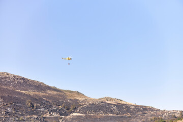 Firefighting helicopter transporting water to extinguish a forest fire. Hazard concept