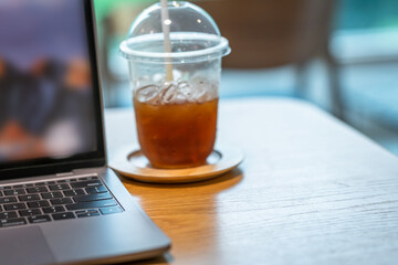 Close-up of ice coffee in cup mug with keyboard laptop computer on wood desk office desk in coffee shop at the cafe,during business work concept