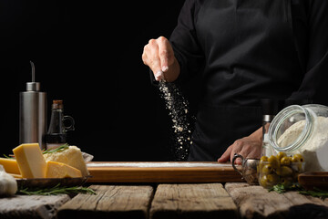 The chef sprinkles flour on a cutting board. Levitation. Ingredients. Cooking pizza, bread, focaccia, pasta. Wooden texture, black background. Restaurant, hotel, cookbook.