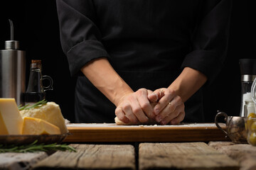The chef kneads the dough. Ingredients. Pizza, pie, focaccia, bread. Restaurant, hotel, culinary blog, recipe book, advertising. Wooden texture. Close-up.