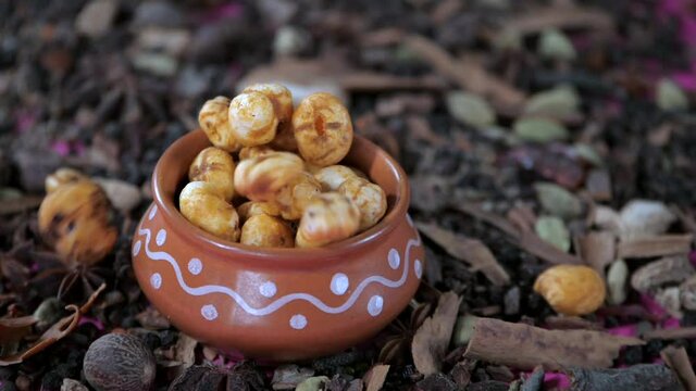 Crispy lotus pop seeds falling inside an earthen pot full of Makhana - healthy snack. Indian spices Javitri  Jaiphal  star anise  cinnamon  and cardamom spread over a table - cooking ingredients  g...