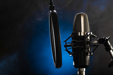 Microphone and pop filter. Blue background and smoke in the background. Minimalism. Close-up. There is no one in the photo. New recording technologies, vocals, radio, television, concert.