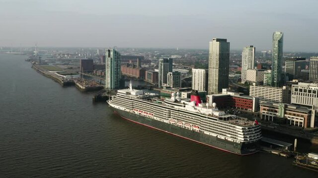 Queen Elizabeth curies ship docked in Liverpool. Cinematic sunset drone shot with Liverpool city skyline in background.
