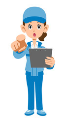 書類を手に指を指す青い作業着の女性の全身
