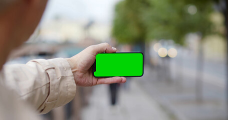 Close up of aged man holding smartphone with blank green screen outdoors
