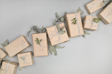 Small gift boxes wrapped in craft paper with dried eucalyptus leaves on solid gray background....