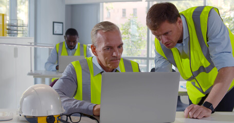 Two male architects working on laptop in office