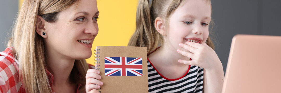 Little girl and mom sitting in front of laptop with english textbooks