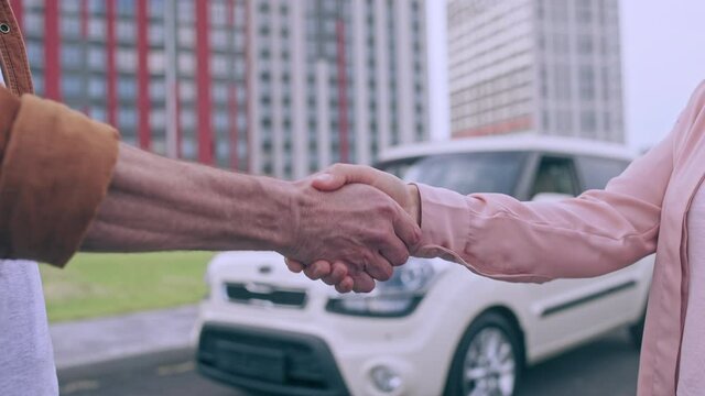 Male giving key to new car owner, shaking hands outdoors, selling automobile