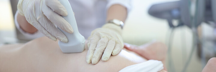 Doctor holding ultrasound probe on breast of female patient in clinic closeup