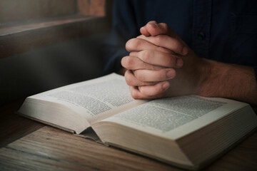 Naklejka premium Man is reading and praying the scripture or holy bible on a wooden table with copy space. Religion, believe Concept.