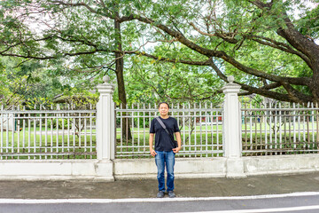 Fototapeta na wymiar Asian Black T-Shirt is standing in front of white vintage fence beside the road in the afternoon time.