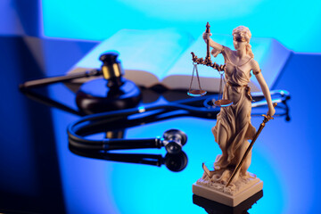 Medical law concept. Gavel, Themis, legal code and stethoscope on the glass table. Blue light.