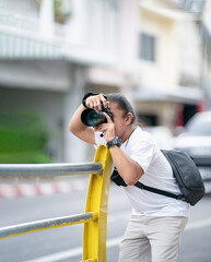 Professional Asian Camera man focus on the image with his mirrorless camera beside the street outdoor field.