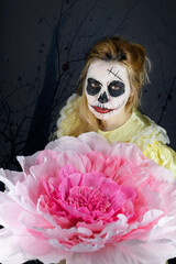 Spooky girl wearing a Halloween costume and dead face makeup. Holding a big pink flower