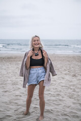 Portrait of beautiful caucasian young woman with blond hair, wearing casual clothes. Walking on the beach with white sand and smiling.