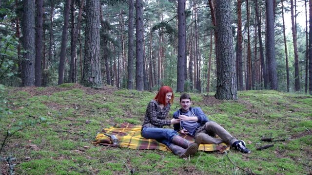 young couple drinking tea from a thermos while sitting on a yellow blanket in the autumn forest