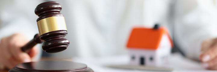 Judge holding wooden hammer near toy little house closeup