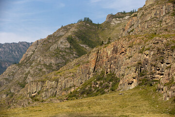 rocks with stones and grass against the background of the summer blue sky
