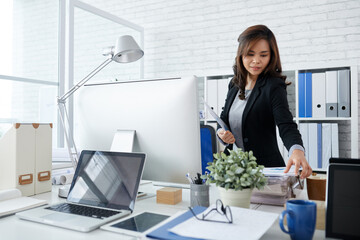 Beautiful elegant businesswoman taking document from stack on her desk when hurrying to meeting