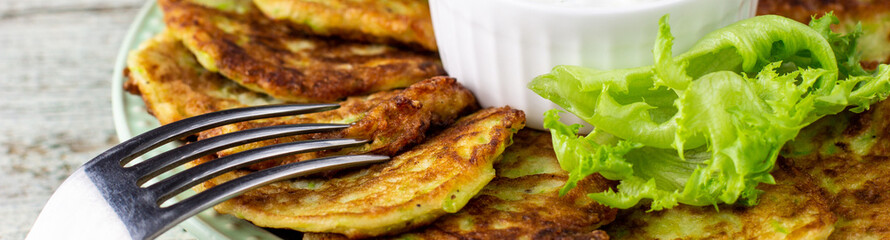 banner of Fritters from zucchini with sour cream sauce and greens. Vegetable pancakes of courgettes with green salad