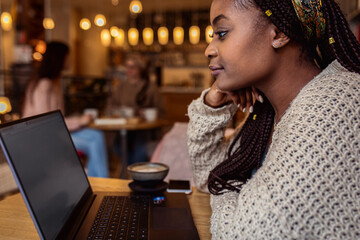Portrait of young woman working on using laptop at coffee shop.