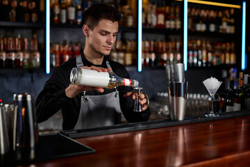 Bartender in apron adds ingredient to shaker