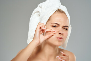 woman with bare shoulders squeeze pimples on her face towel on her head light background