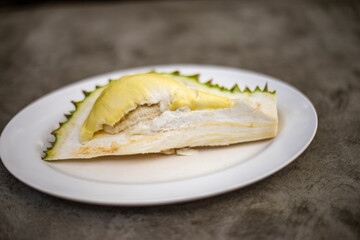 Ripe durian with peel is placed on a white plate. Blurred background.