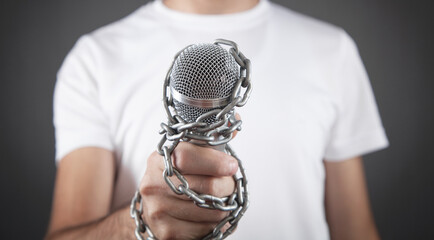 Human hand holding microphone tied with chains.
