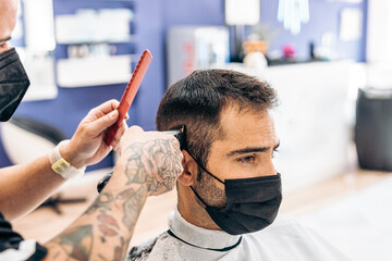 Barber cutting the hair of a client with a mask with a machine