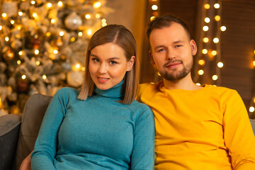 Fototapeta premium Young loving couple celebrating Christmas at home. Young man and his attractive girlfriend in a home interior with a Christmas tree.