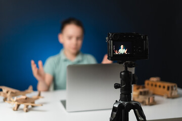 Kid blogger filming video on camera using the laptop, indoors. Online reviewing. Promoting eco wooden toys. Kid recording his gameplay for vlog.