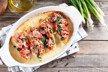 Chicken breast in creamy garlic sauce in baking dish on a wooden table. Healthy diet food. Top view, flat lay, copy space