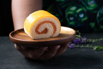 Orange roll cake in wooden plate on black background
