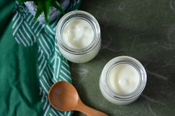 white yogurt in two glass jars on green background
