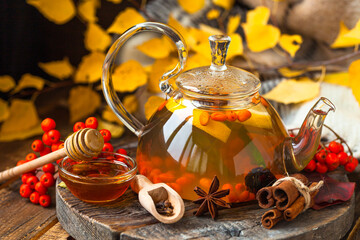 Fototapeta na wymiar Concept of warm autumn beverage. Hot herbal tea with sea buckthorn and spices: anise, cinnamon, clove, cardamon. Cozy home atmopshere, aromatherapy. Wooden background, yellow fall leaves as decor.