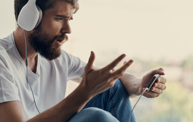 a man in headphones on the windowsill near the window listens to music