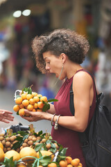 Excited curly young woman buying fresh ripe delicious Vietnamese sapodilla at local market